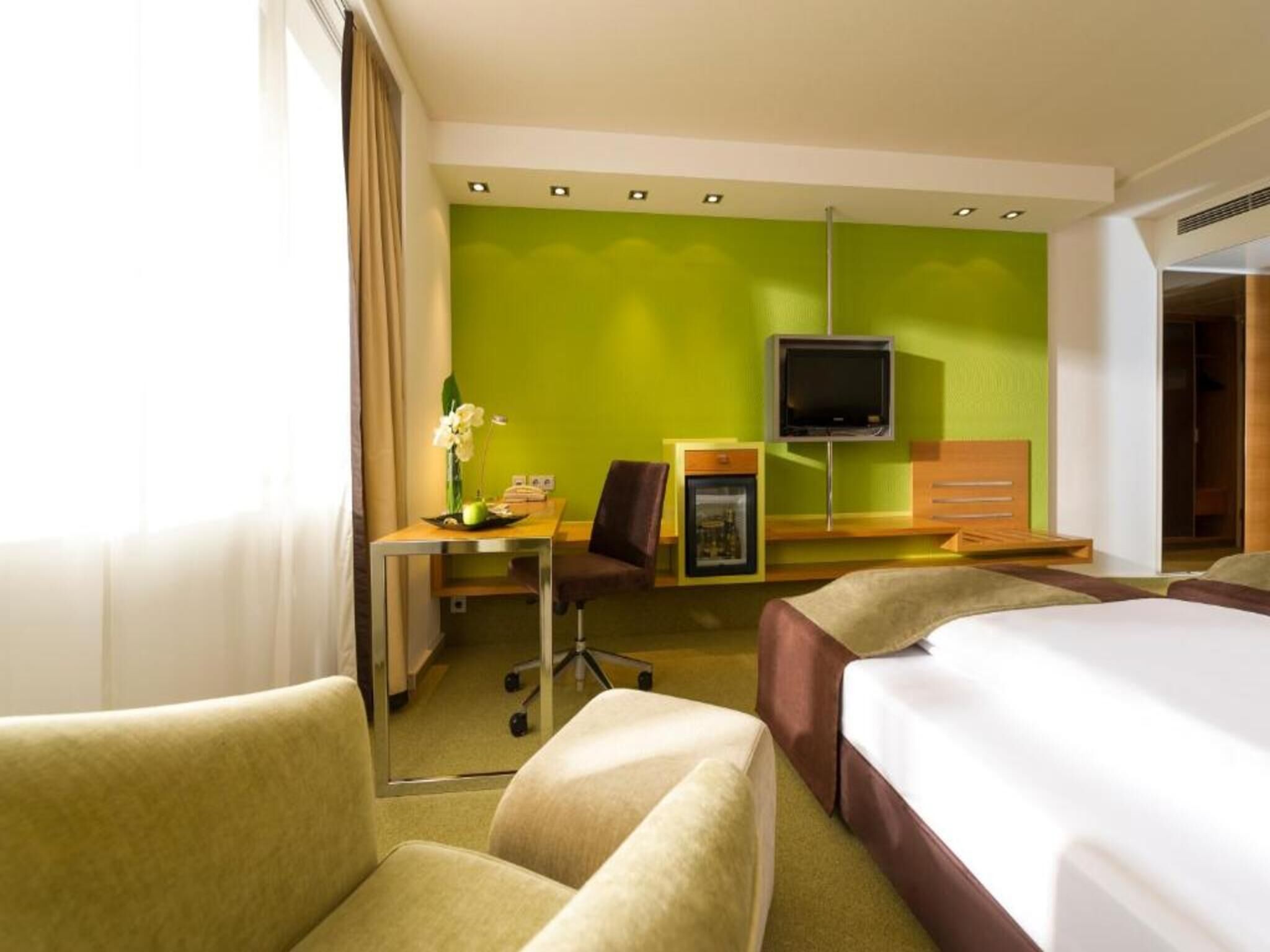 Une chambre d’hôtel avec un lit, un bureau, une chaise, une télévision et un mur vert.
