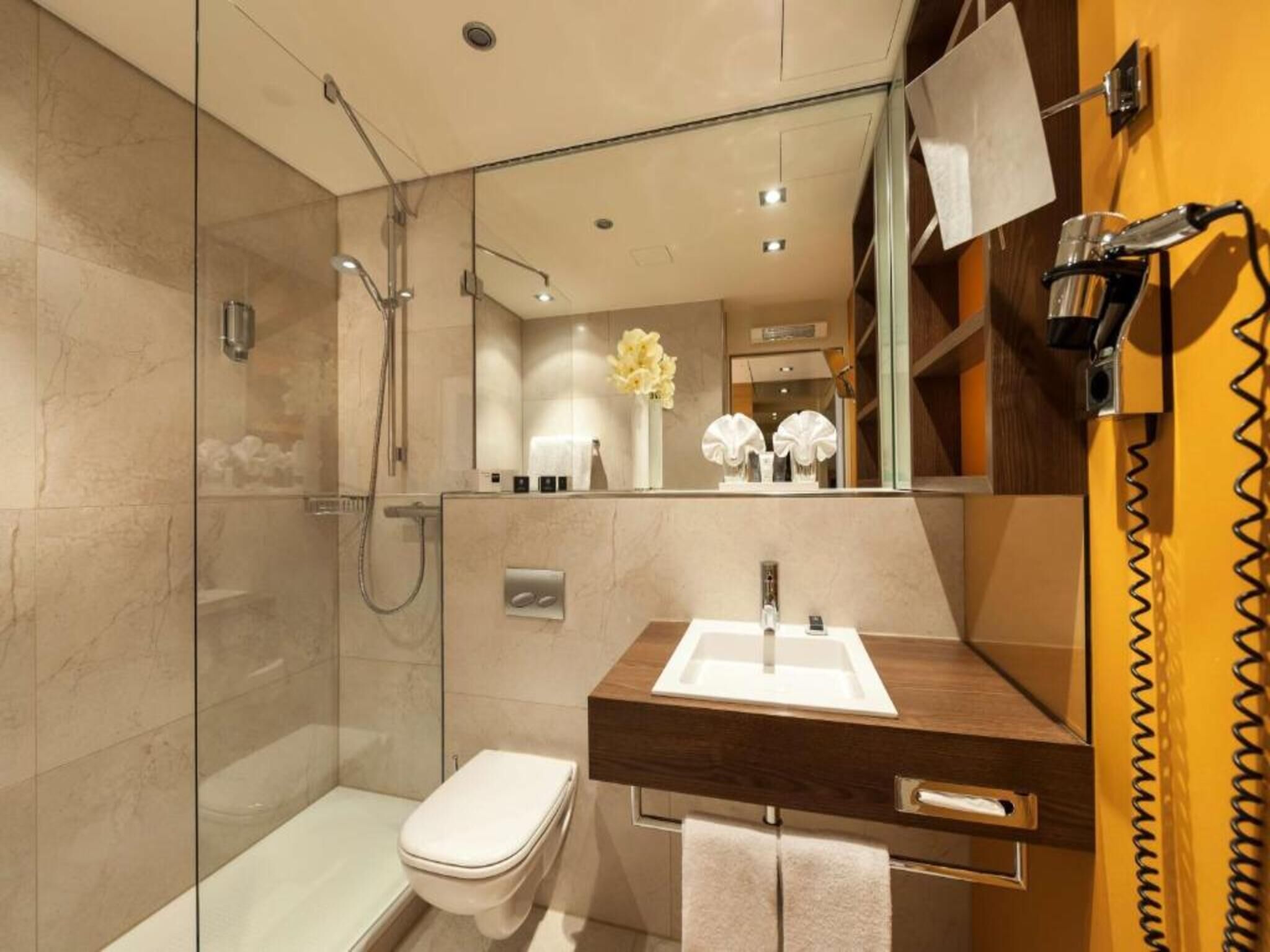 Un baño moderno con ducha de vidrio, inodoro blanco, tocador de madera con lavabo y espejo.