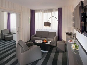 Ein modernes Wohnzimmer mit einer Couch, einem Sessel, einem Couchtisch und einem an der Wand befestigten Fernseher.
