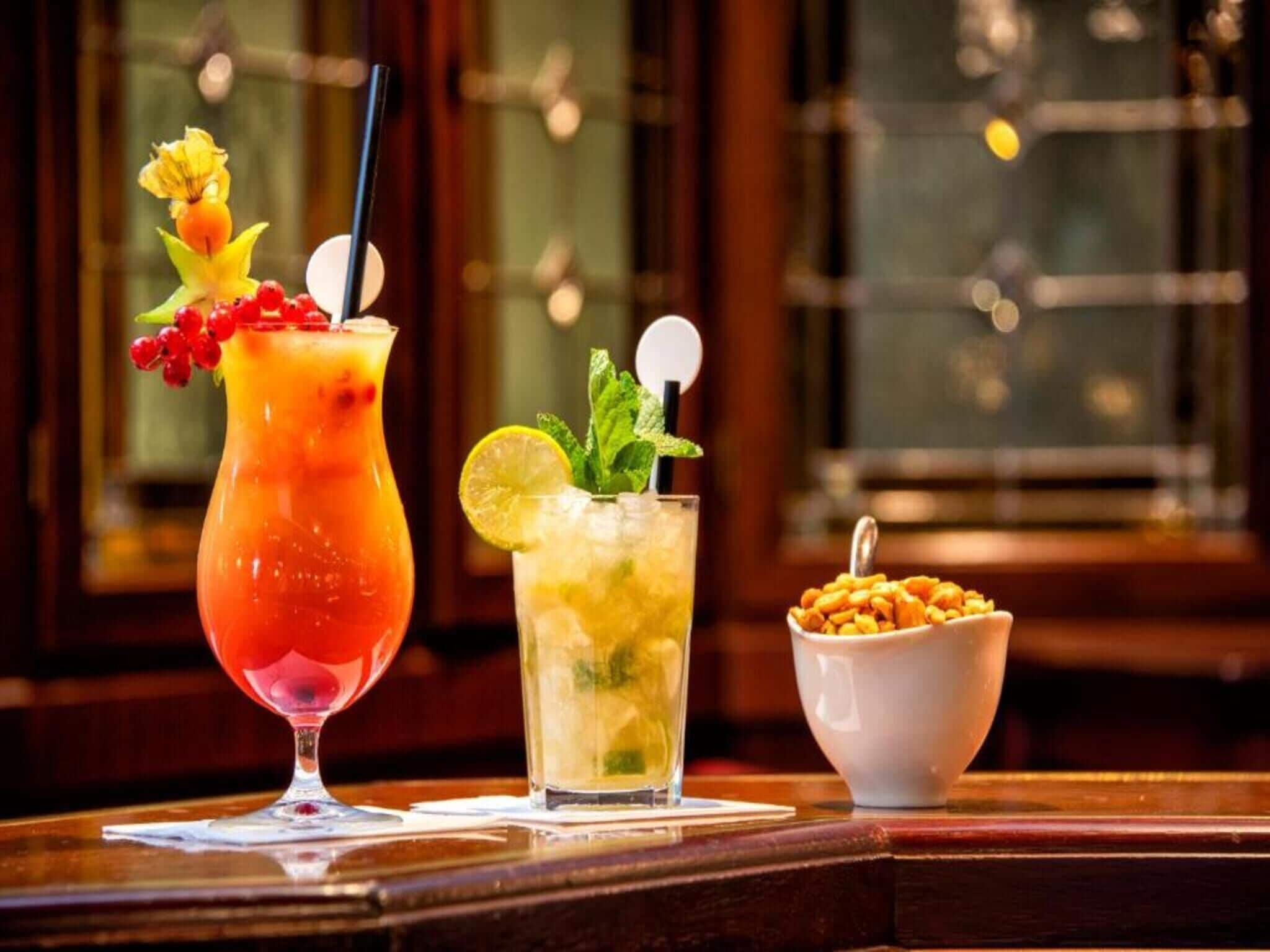 Two drinks on a bar counter with a bowl of cereal beside them.