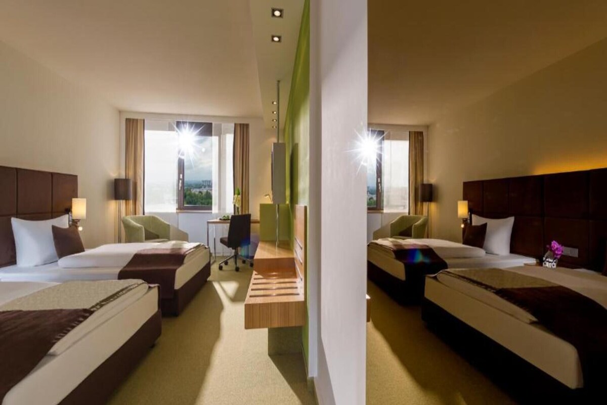 Ein Hotelzimmer mit zwei Betten, einem Schreibtisch und Blick auf die Stadt.