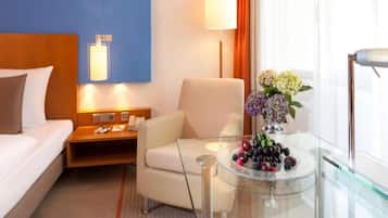 Ein Hotelzimmer mit einem Bett, einem Schreibtisch, einem Sessel, einer Lampe und einem Glastisch mit Obst.