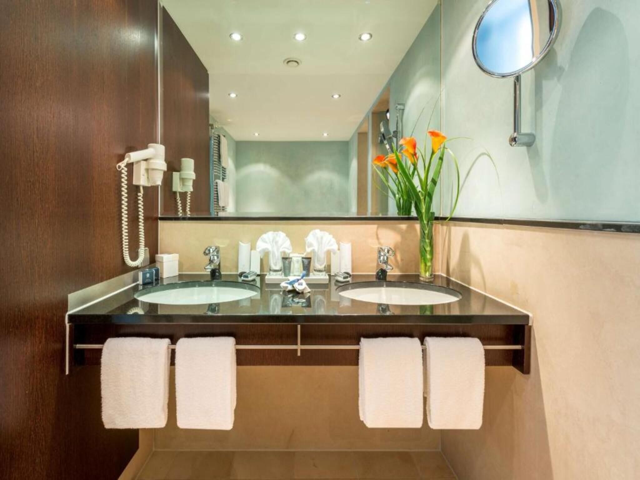 A modern bathroom with two sinks, a mirror, and a vase with flowers.