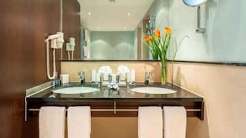 A modern bathroom with two sinks, a mirror, and a vase with flowers.
