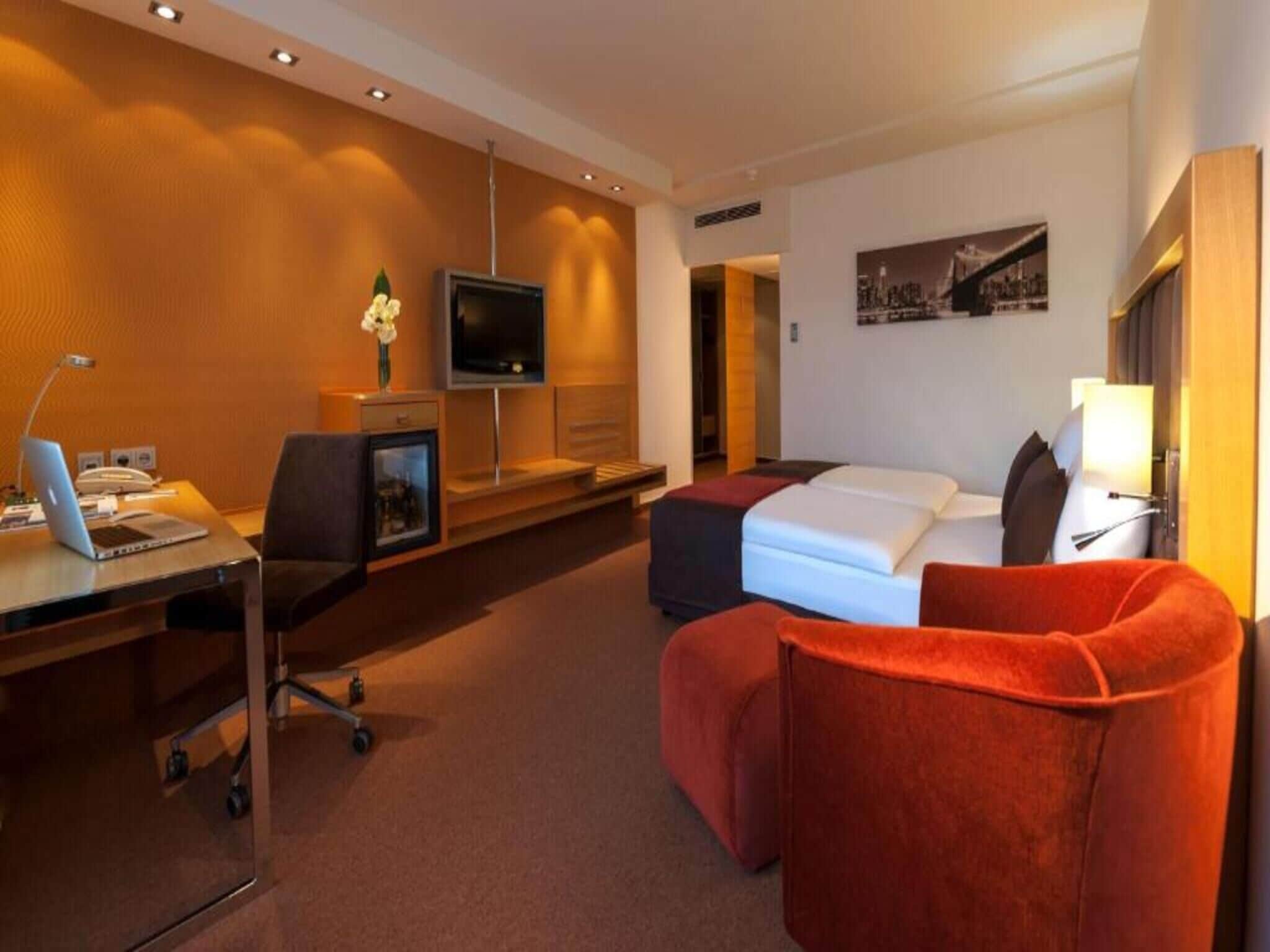 Une chambre d’hôtel avec un bureau, un lit, une télévision et un fauteuil rouge.