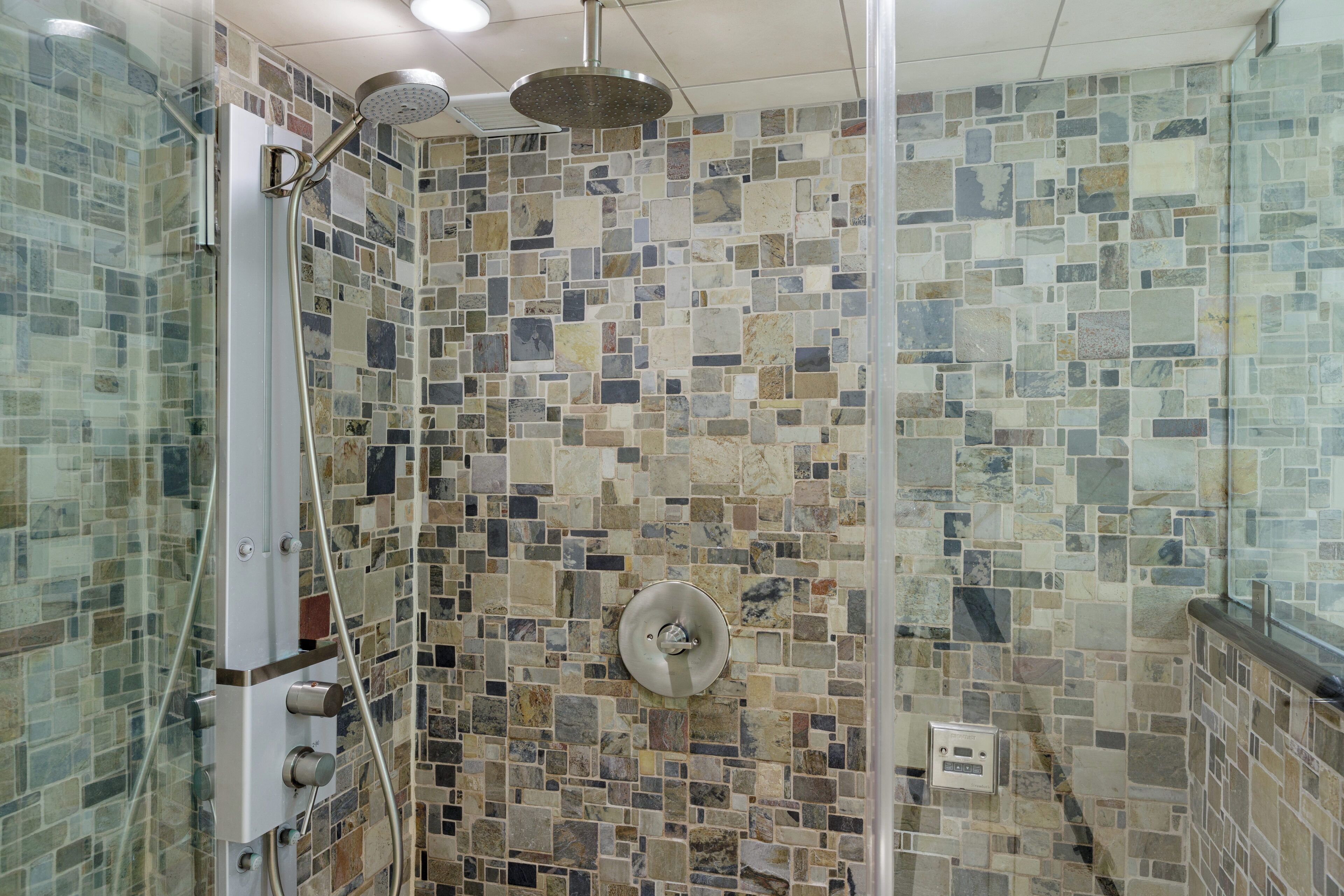 A shower with a mosaic tile wall, a glass enclosure, and a handheld showerhead.