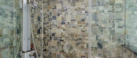 A shower with a mosaic tile wall, a glass enclosure, and a handheld showerhead.