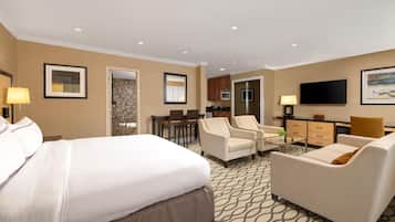A hotel room with a large bed, two armchairs, a desk, a television, and a dining area.