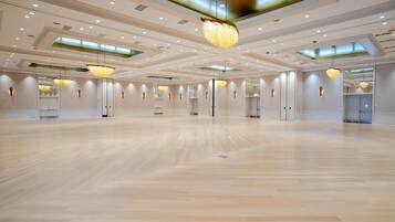 Un salón de eventos amplio en un hotel, con piso de madera lustrosa, iluminación empotrada y candelabros modernos.