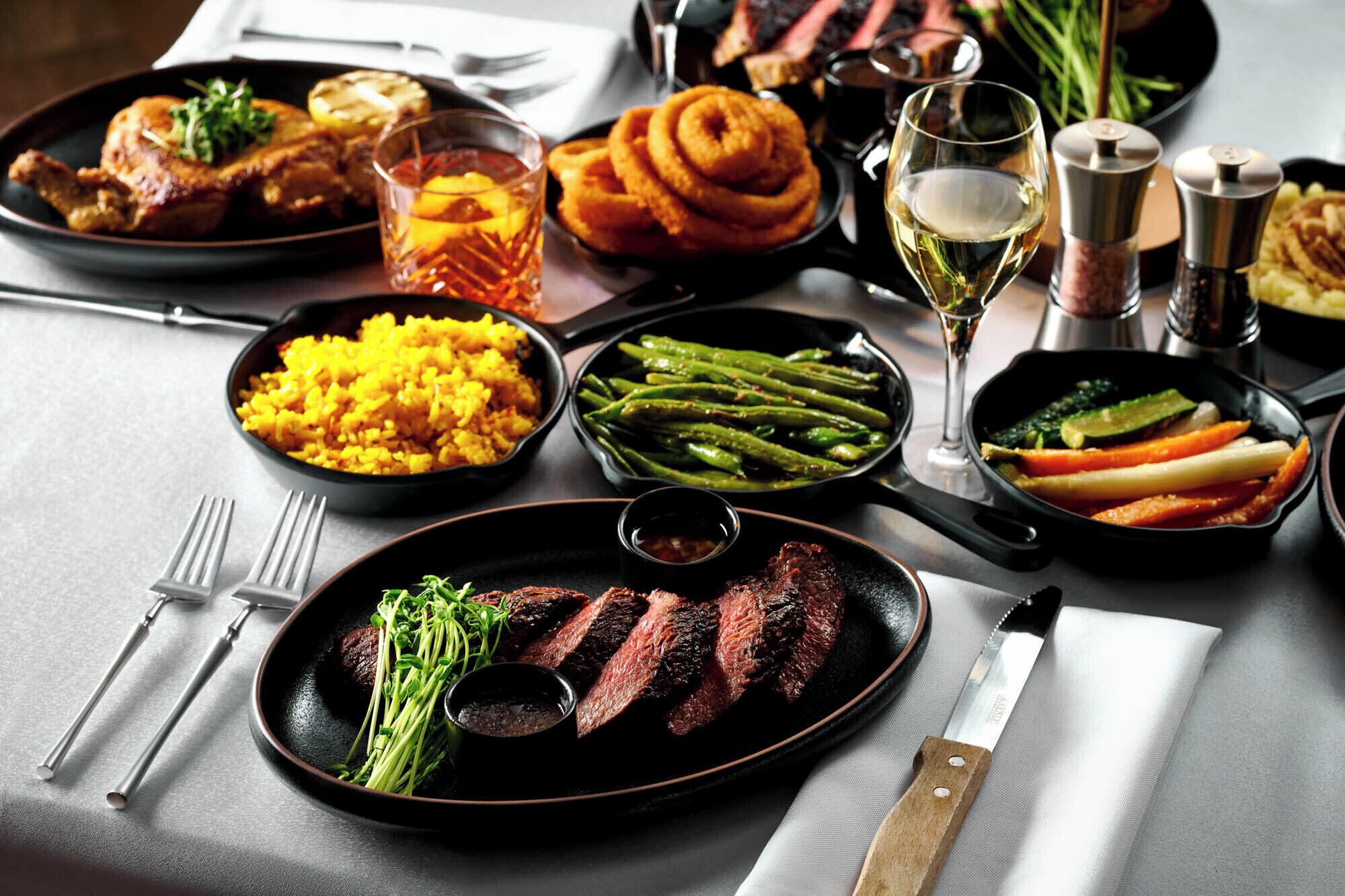 Ein Tisch ist reichhaltig mit verschiedenen Speisen gedeckt, darunter Steak, Spargel und Reis.