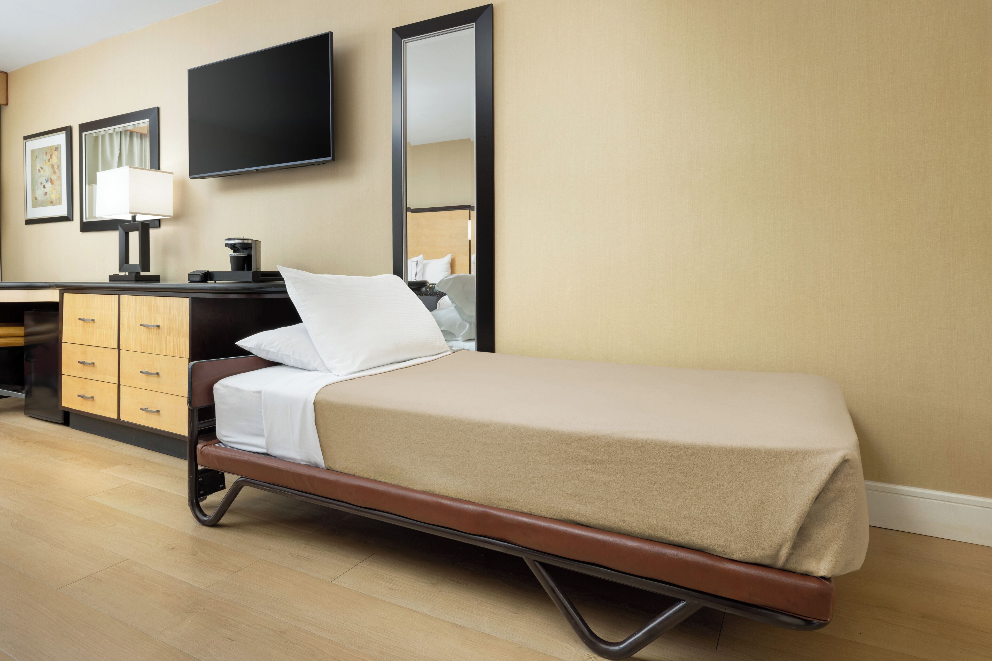 Ein Hotelzimmer mit einem Bett, einem Schreibtisch mit Lampe, einem Flachbildfernseher und einem Spiegel.