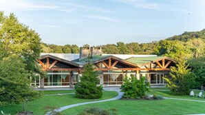 A modern building with a stone facade and wooden beams, surrounded by a well-maintained lawn and trees. - Sleepy Hollow Hotel, a Dolce by Wyndham (Tarrytown)