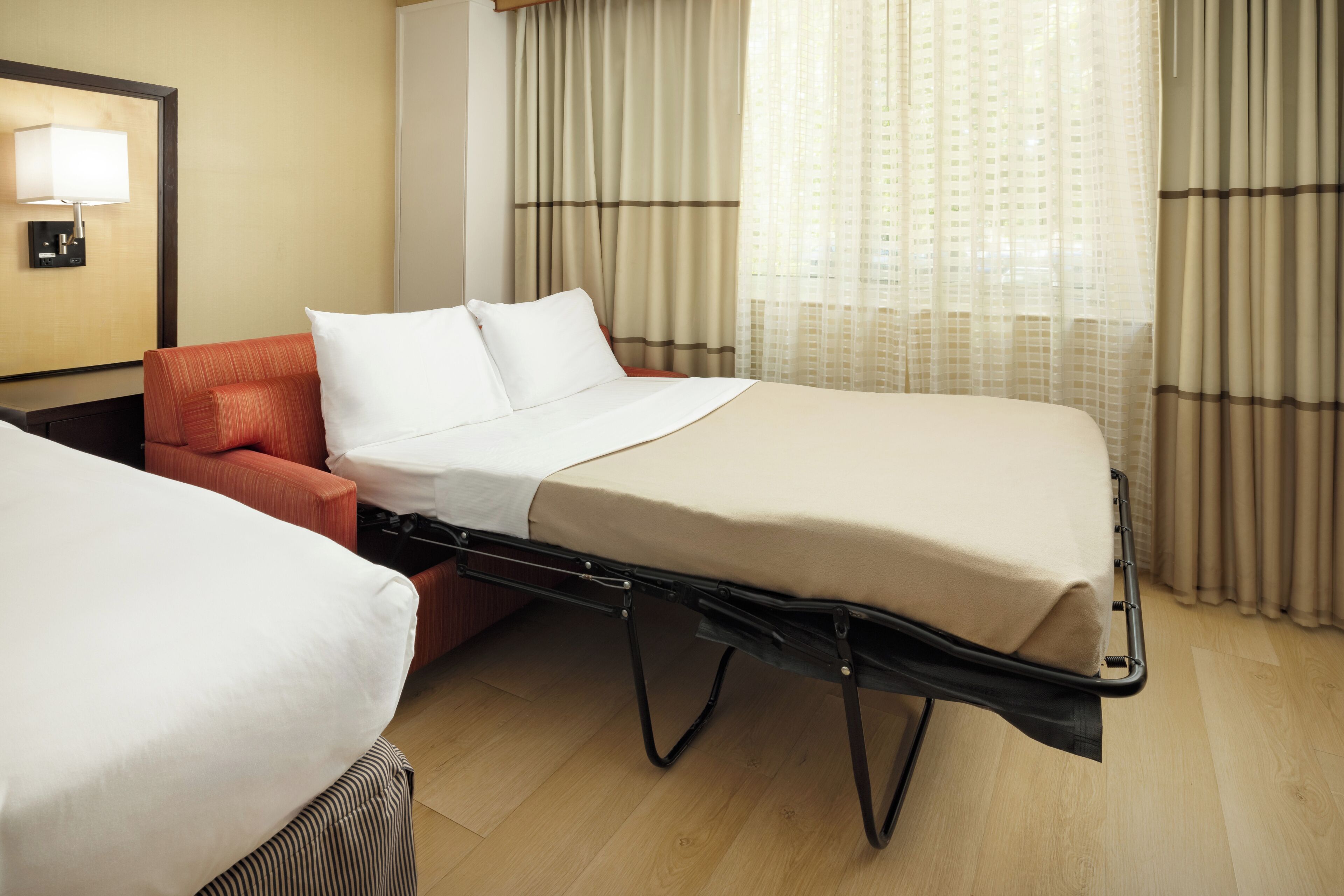 A hotel room with a bed, a chair, a lamp, and curtains.