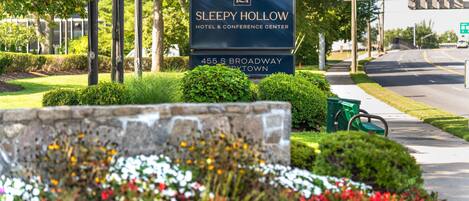 Schild für das Sleepy Hollow Hotel & Conference Center in der South Broadway 455, mit hervorgehobenem Logo, umgeben von gepflegter Bepflanzung und einer gut einsehbaren Straße im Hintergrund.