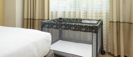 Habitación de hotel con cama, cuna con cubierta estampada y cortinas.
