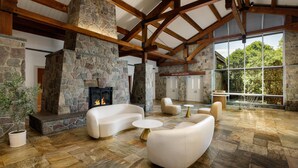 A spacious room with a stone fireplace, white sofas, and a large window offering a view of the outdoors. - Sleepy Hollow Hotel, a Dolce by Wyndham (Tarrytown)