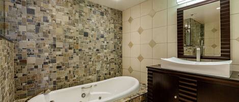 Un baño con pared de mosaicos, una bañera independiente, un tocador con espejo y una vela encendida.