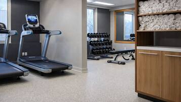 Un gimnasio con cintas de correr, mancuernas y un banco.