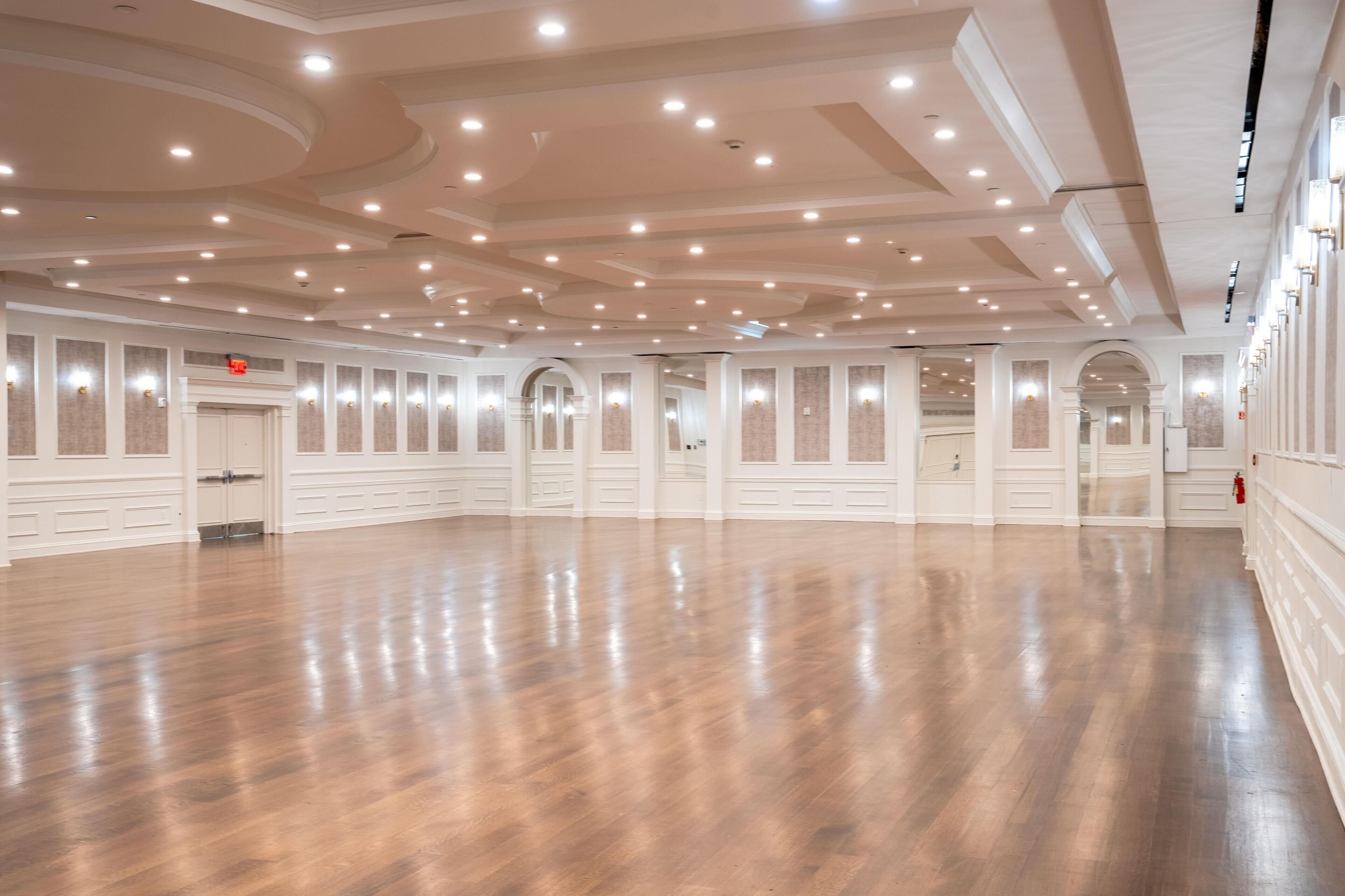 Un vaste hall doté d’un plancher en bois poli, de murs blancs et d’une série de spots encastrés au plafond.