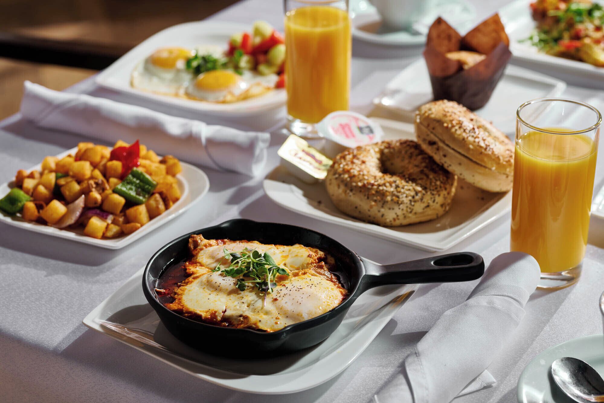 A breakfast setting with various dishes, including eggs, a skillet dish, and a bagel, on a table.
