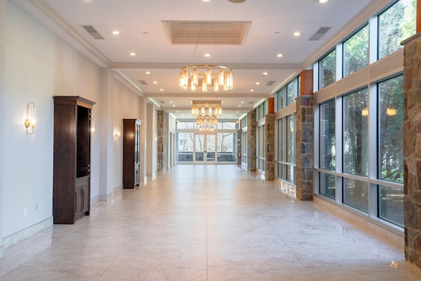 A spacious corridor with stone walls, large windows, and a central chandelier.