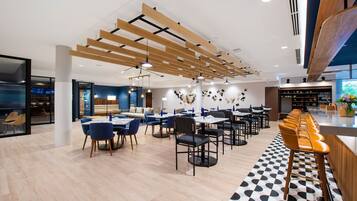 A modern restaurant with wooden ceiling beams, a checkered floor, and a long bar with orange stools.