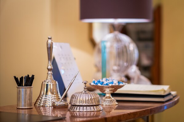 A table with various silverware, a bell, a bowl of candies, and a lamp in the background.