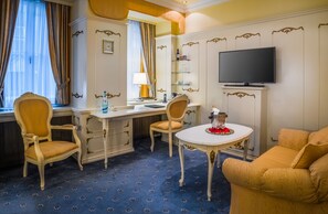 A hotel room with a desk, two chairs, a small table with a decorative centerpiece, a television, and a large window with curtains.