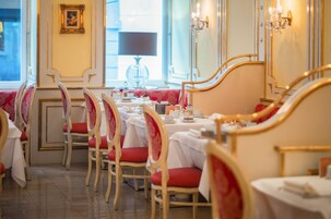A dining area with tables set for service, chairs with red cushions, and a chandelier.