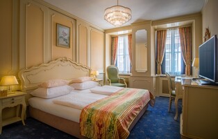 Quarto de hotel com uma cama grande, uma escrivaninha, uma cadeira, uma televisão e um lustre.