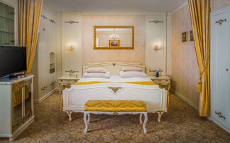 Um quarto luxuoso com uma cama grande, um banco, uma televisão e um espelho.