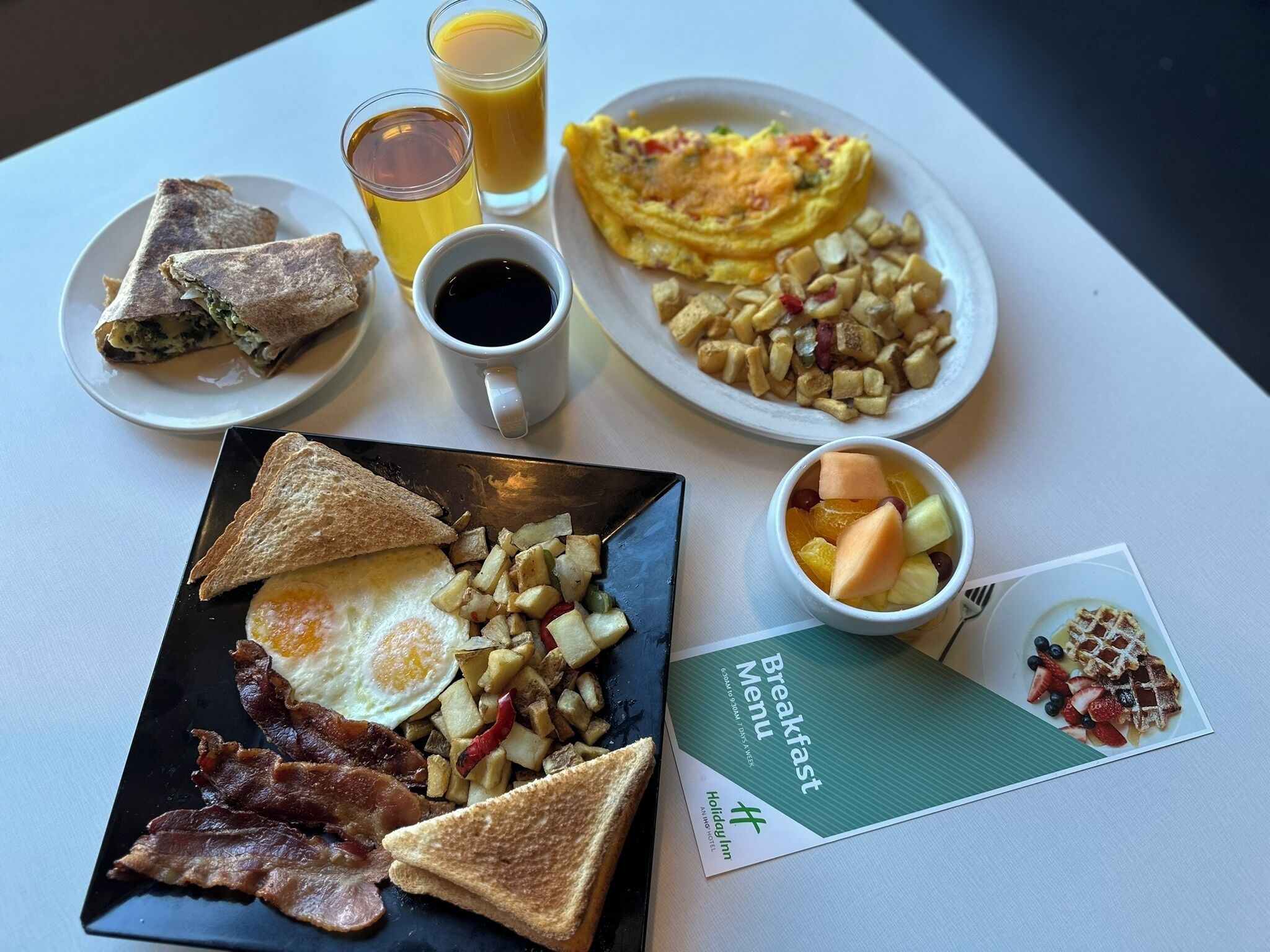A breakfast spread with toast, eggs, bacon, potatoes, and fruit on a table.