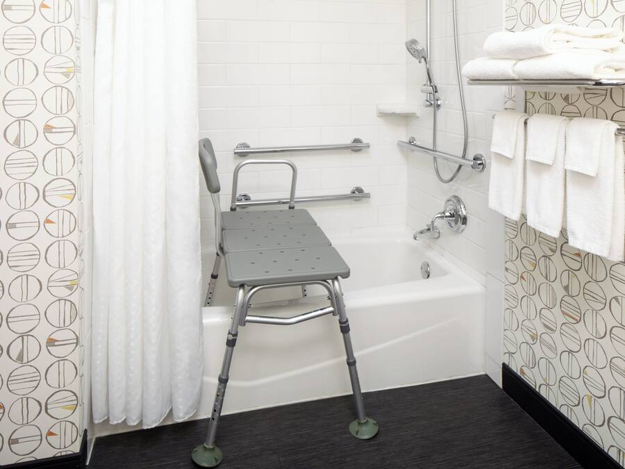 Ein Badezimmer mit einer Badewanne, einer Dusche, einer Haltestange und einem Handtuchhalter.