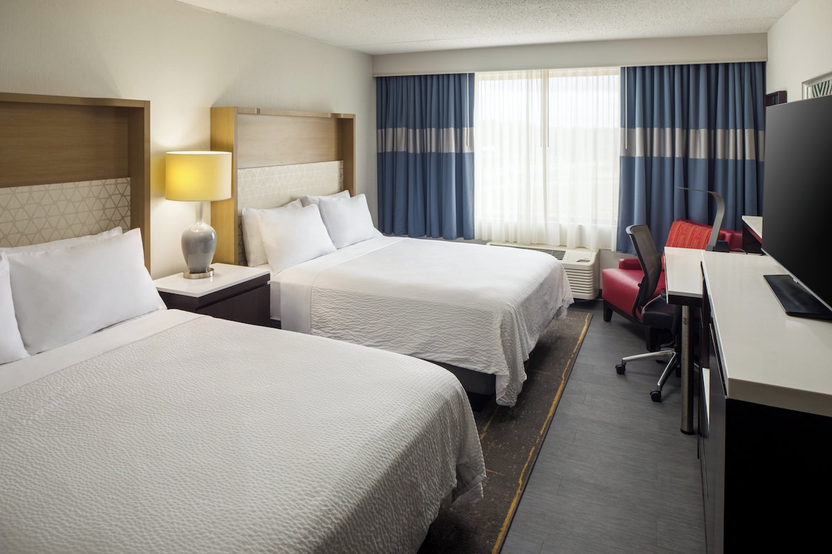 Une chambre d’hôtel avec deux lits, un bureau avec un ordinateur et une télévision.