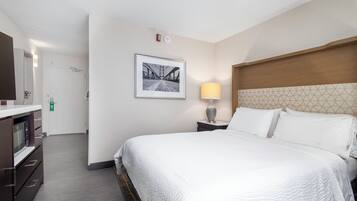 A hotel room with a bed, a bedside lamp, a framed picture on the wall, and a microwave in the corner.