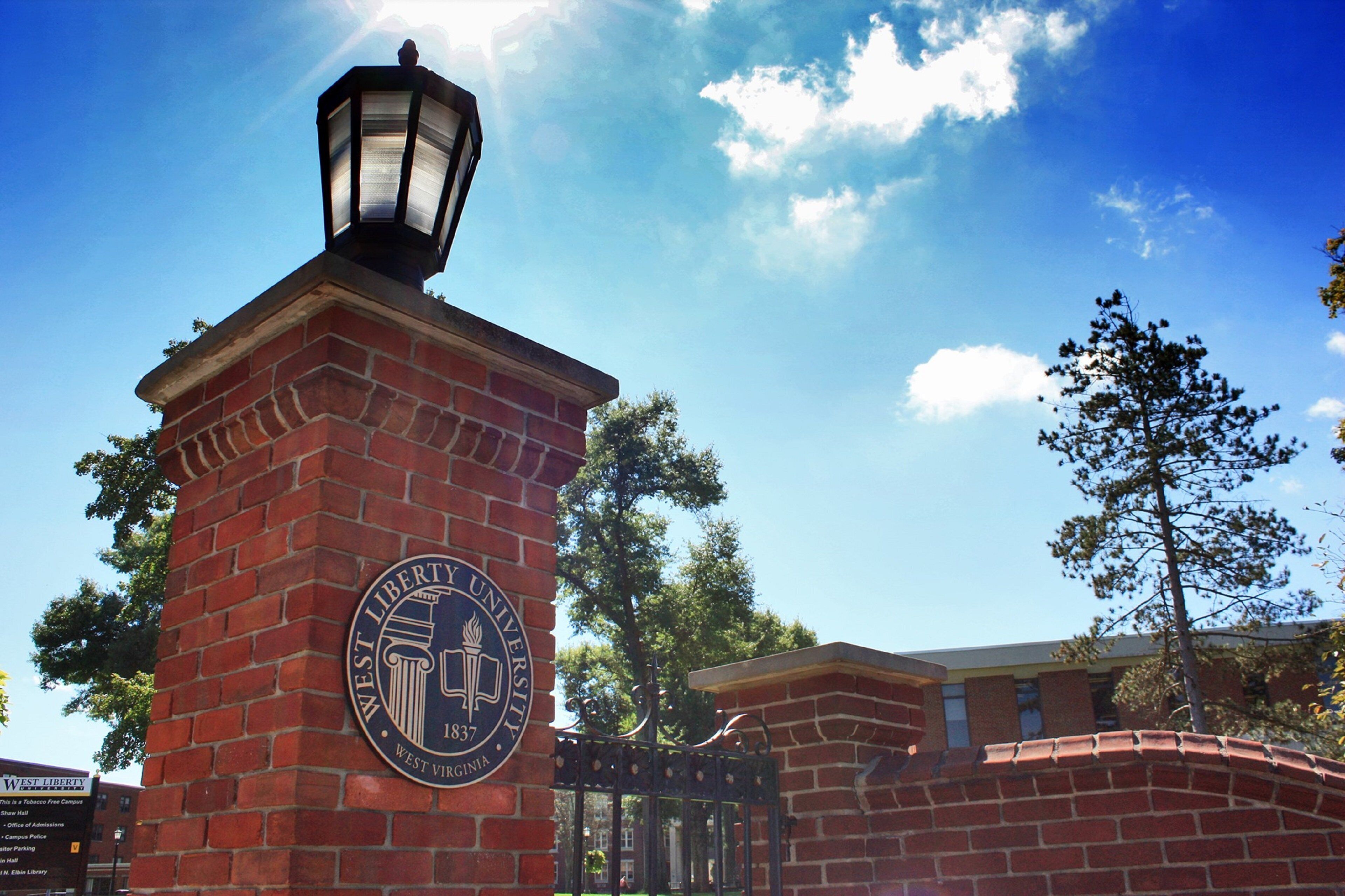 A brick entrance with a sign for West Liberty University, a lamp post, and a clear blue sky.