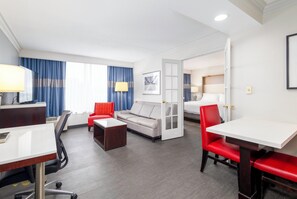 A hotel room with a desk, two chairs, a sofa, a coffee table, and a bed. - Holiday Inn Weirton - Steubenville Area by IHG (Weirton)