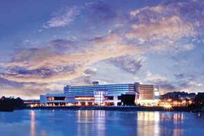 A waterfront hotel with multiple buildings, a reflective pool, and a city skyline in the background. - Holiday Inn Weirton - Steubenville Area by IHG (Weirton)