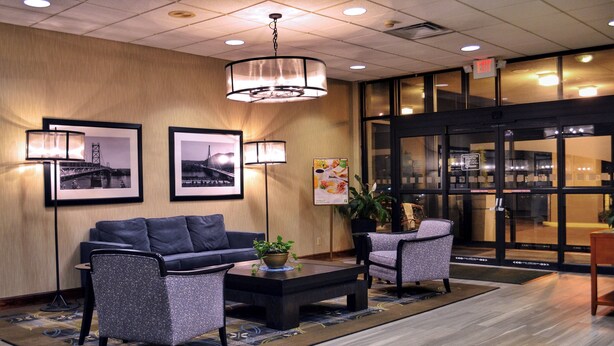 A lobby with a sofa, two armchairs, a coffee table, and framed pictures on the wall. - Holiday Inn Weirton - Steubenville Area by IHG (Weirton)