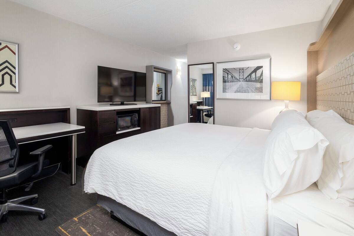A hotel room with a large bed, a desk with a chair, a television, and a mirror.