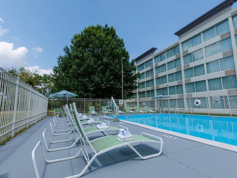 A swimming pool area with lounge chairs, a fence, and a building with large windows.