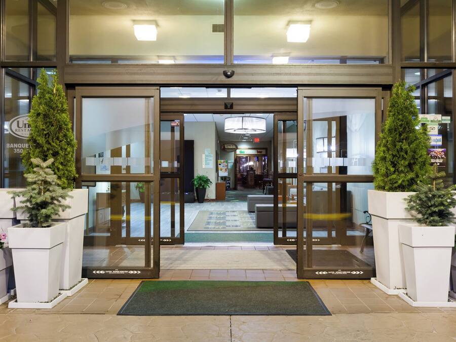 Entrada d'hotel amb portes dobles, plantes en testos i interior visible que inclou una zona de recepció i una escala.