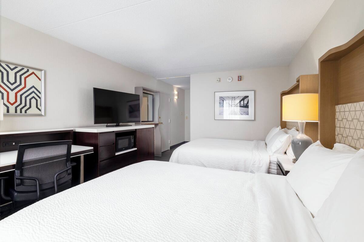 A hotel room with two beds, a desk with a chair, a television, and a lamp.