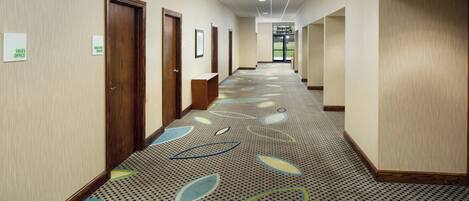 A hotel hallway with a patterned carpet, wooden doors, and signs indicating the sales and business office locations.