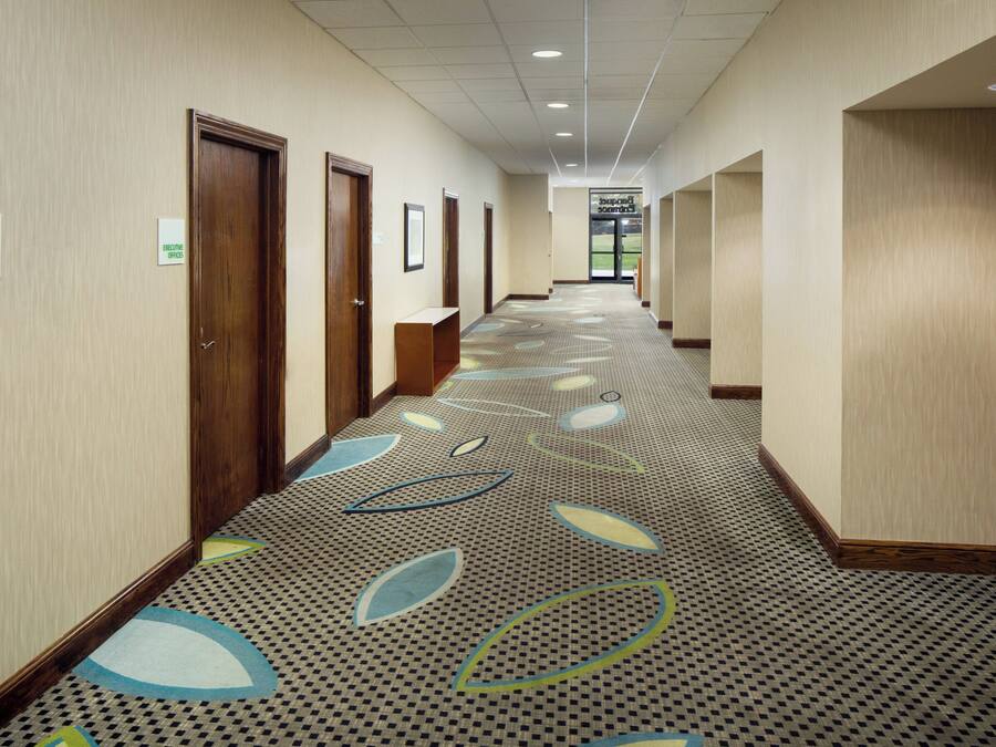 Un pasillo de hotel con alfombra estampada, puertas de madera y carteles que señalan la ubicación de las oficinas de ventas y negocios.