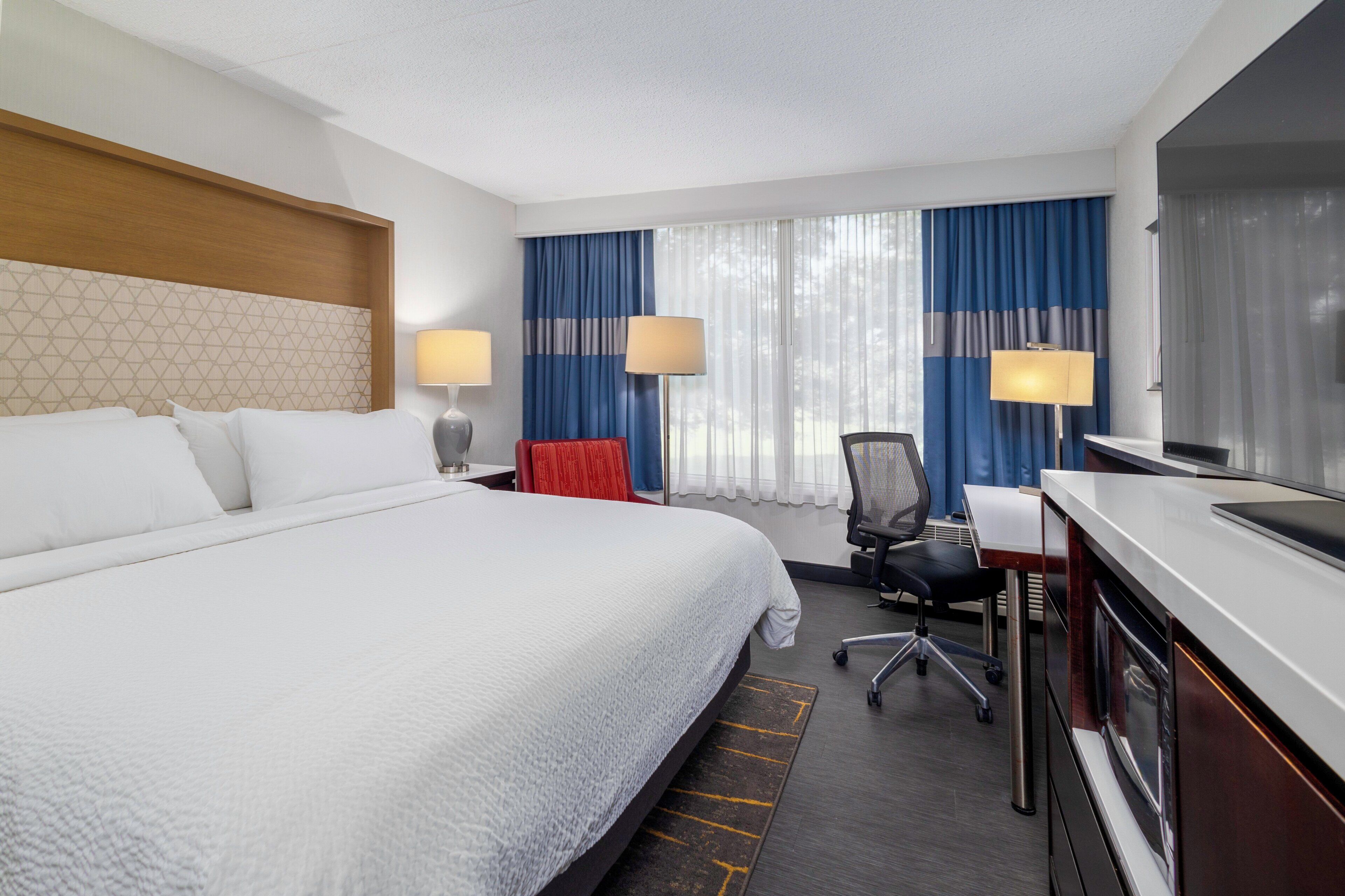 Habitación de hotel con una cama grande, un escritorio con silla, dos lámparas y un televisor.