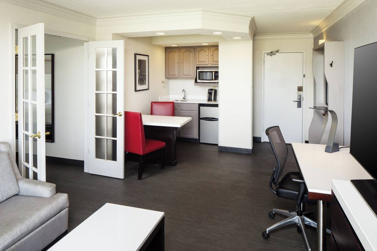 A compact hotel room with a kitchenette, a dining area, and a seating area.