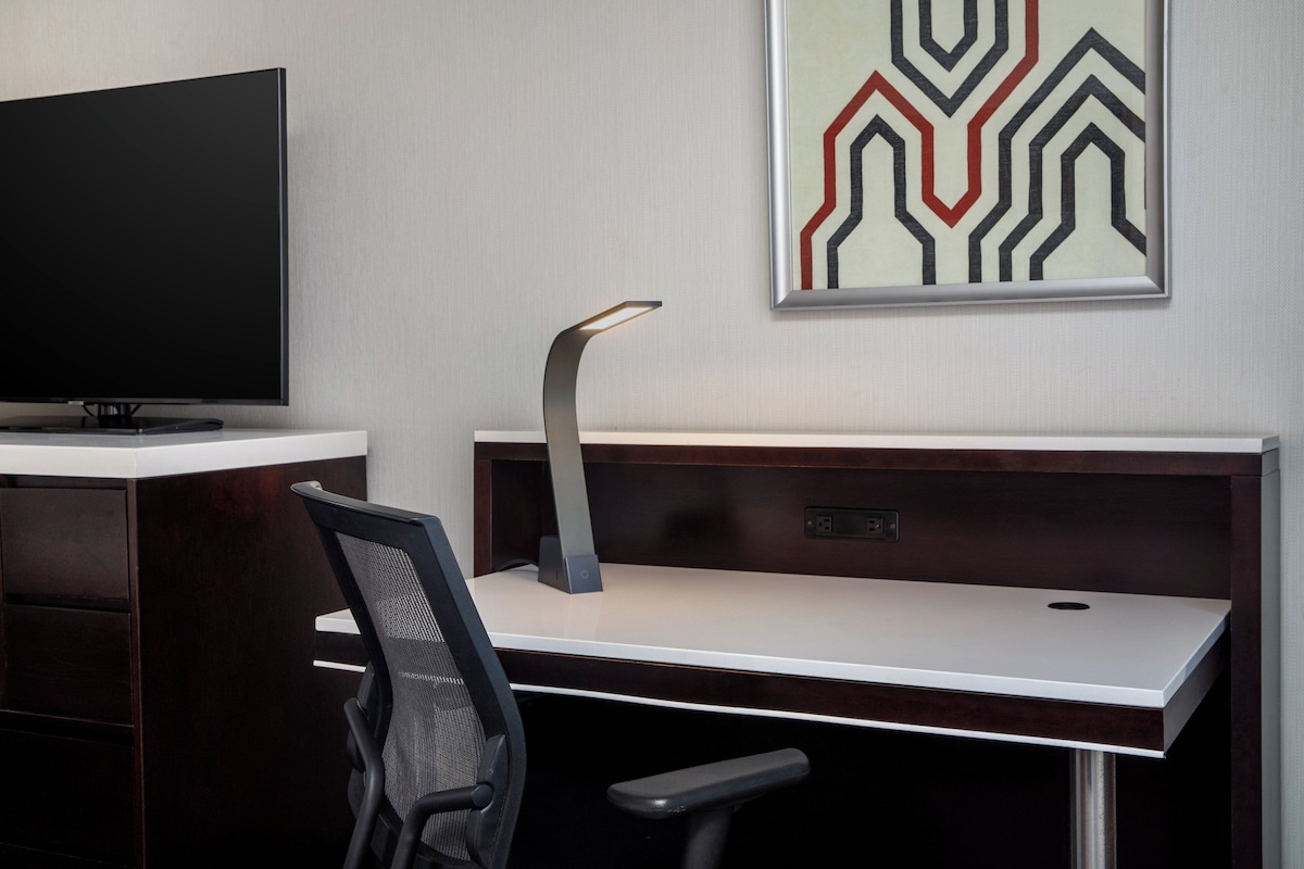 Un bureau moderne, doté d’un téléviseur à écran plat, d’une lampe de bureau élégante et d’une œuvre d’art abstraite encadrée accrochée au mur.