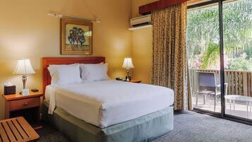 A hotel room with a large bed, two bedside tables with lamps, a painting on the wall, and a balcony with a view of greenery.