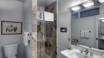 Un baño moderno con ducha envuelta en vidrio, un lavabo blanco y una obra de arte enmarcada en la pared.